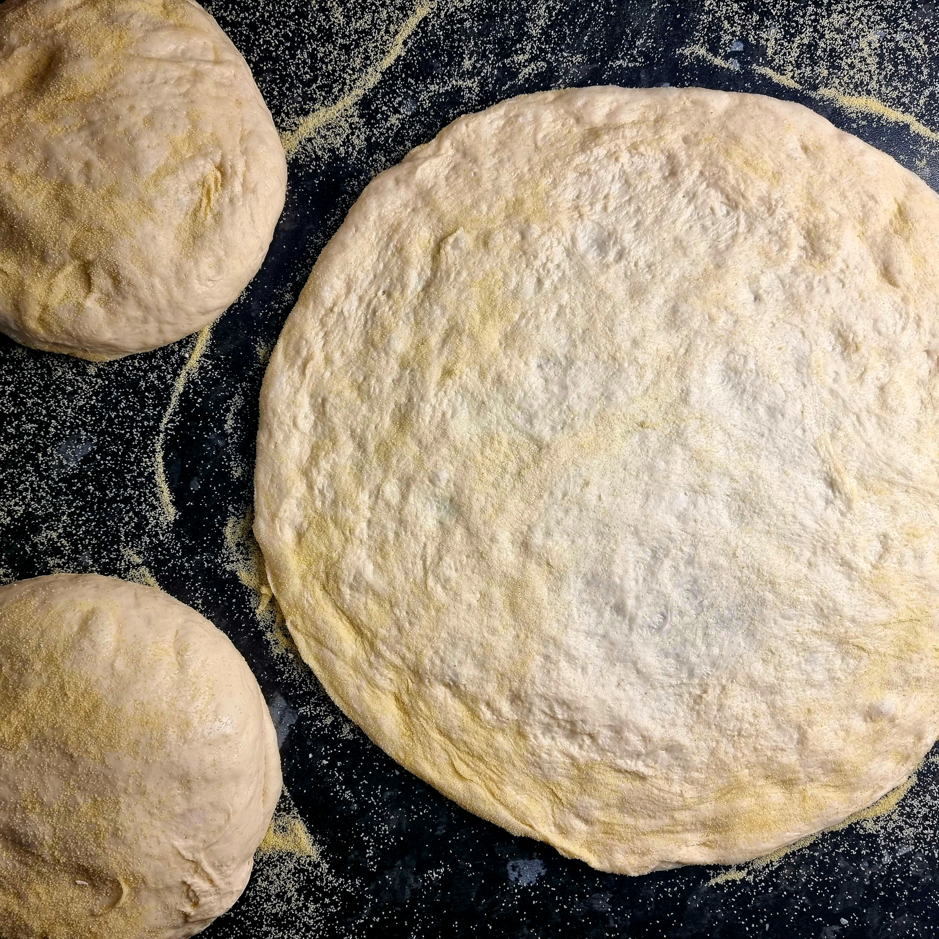 two dough balls and homemade and handstretch pizza dough with a dusting of semolina