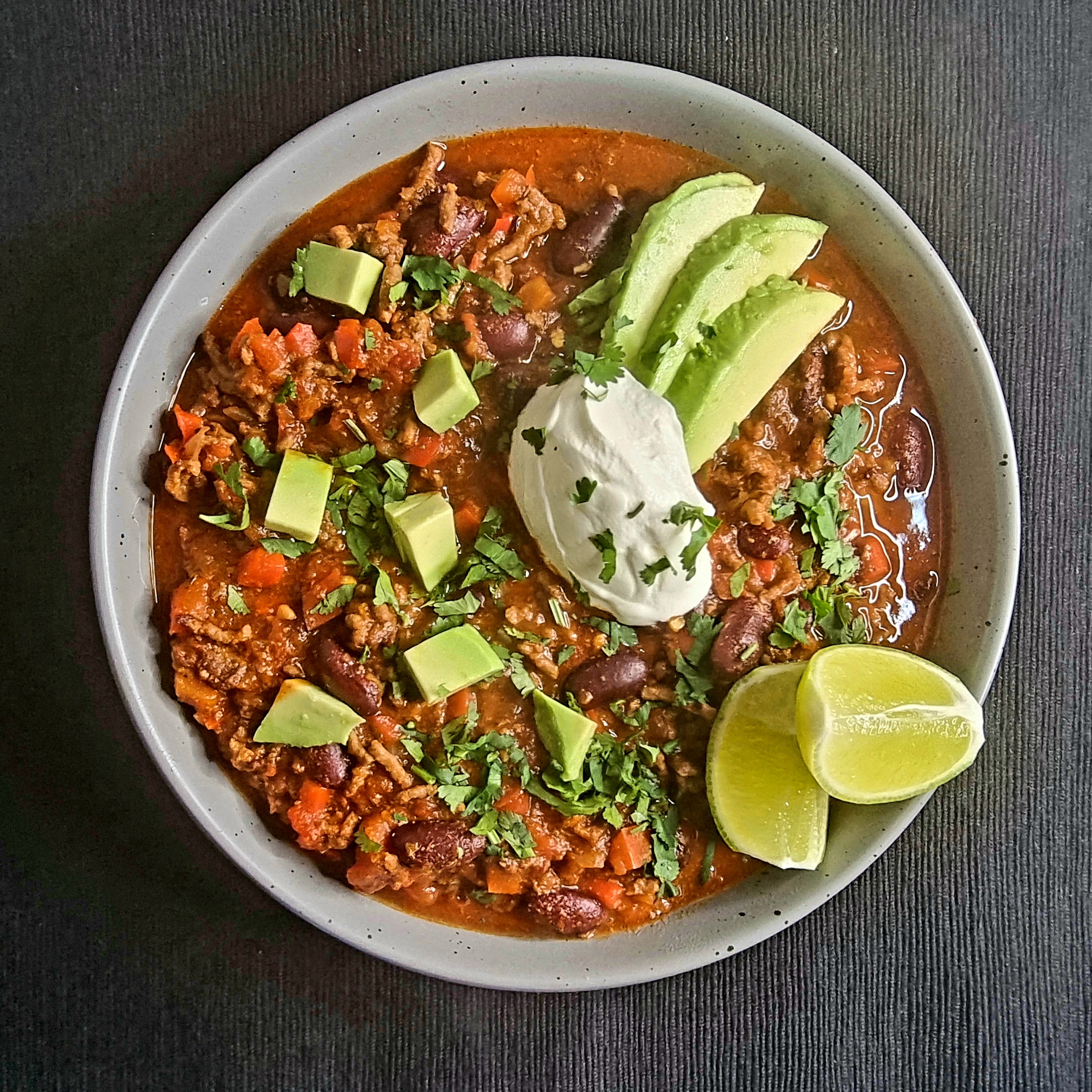 Beef Chilli with Red Peppers. Garnished with sour cream, avocado, coriander, and lime wedges