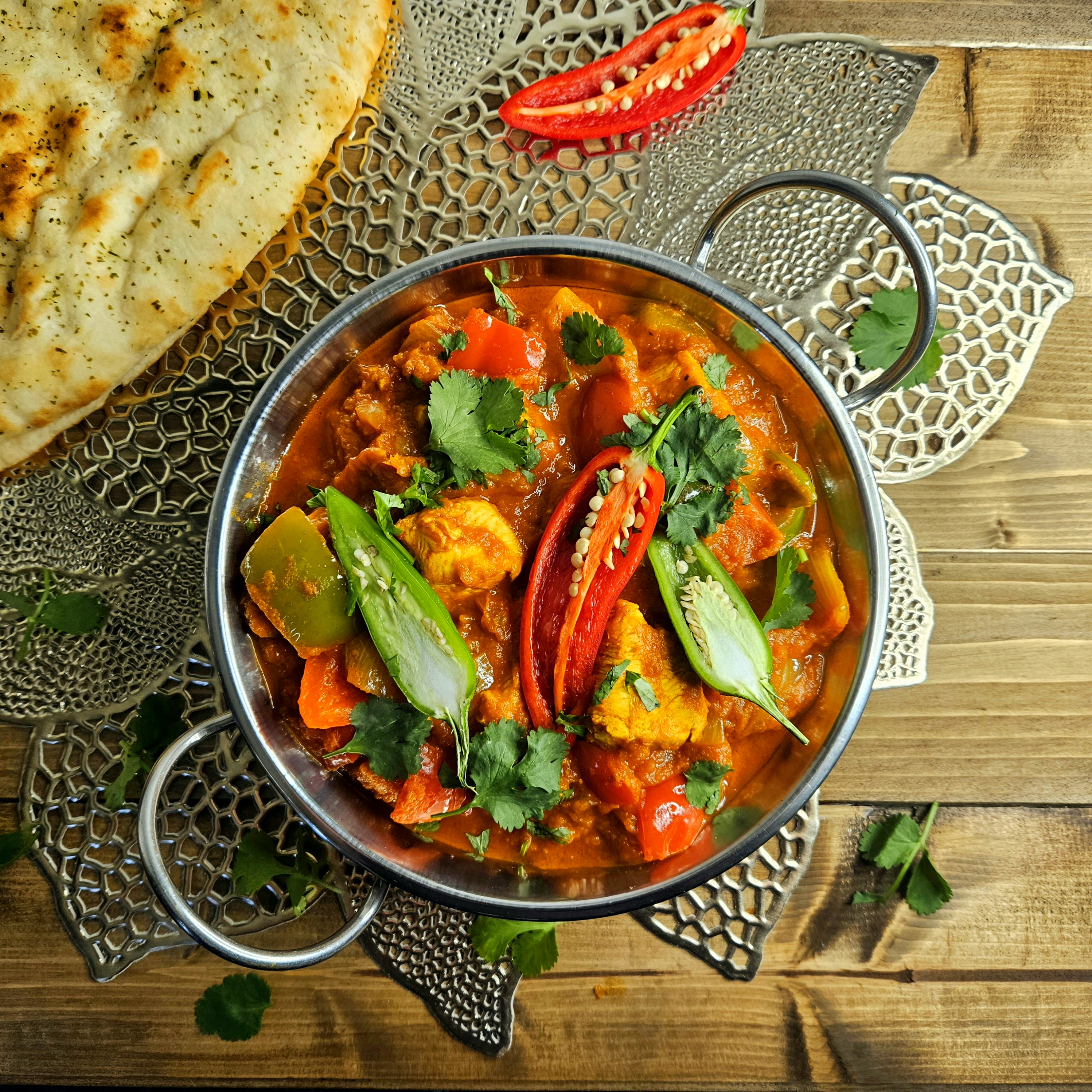 Bowl of chicken jalfrezi, served in a balti dish with corainder, naan bread, and chilli