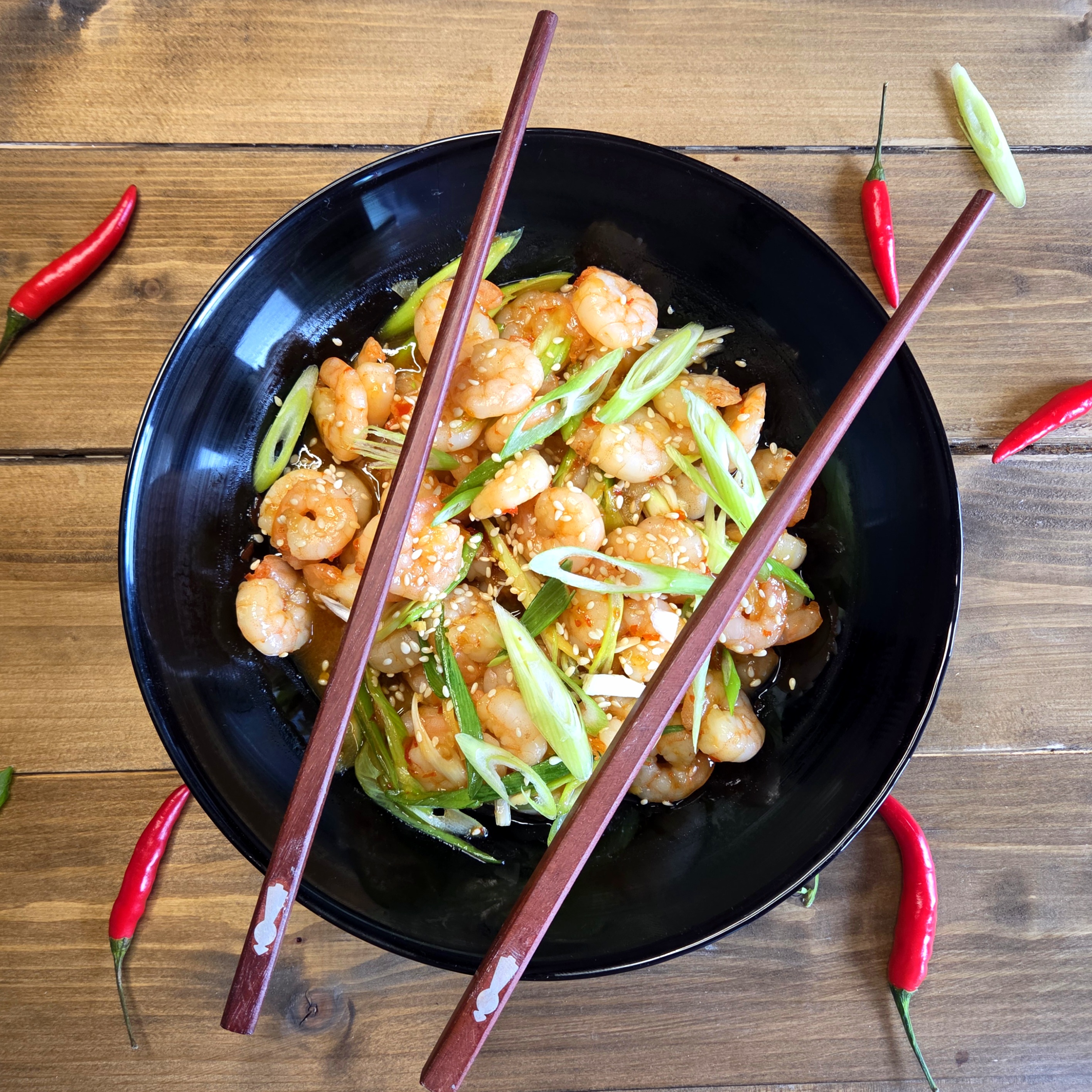Thai sweet chilli prawns in a black bowl with chillies and chopsticks